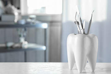 Tooth shaped holder with professional dentist tools on table in clinic. Space for text