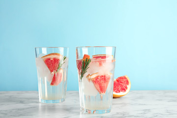 Glasses of infused water with grapefruit slices on table against color background. Space for text
