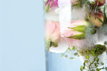 Glass of water with ice cubes and flowers on color background, closeup. Space for text