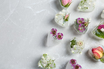 Heart shaped ice cubes with flowers on grey background, flat lay. Space for text