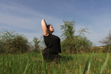 Body positive, yoga, confidence, high self esteem, meditating. Young calm overweight woman doing yoga at summer meadow. obesity, wellness, outdoor activity and health