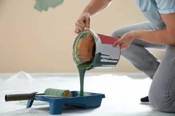 Young man pouring paint from bucket into tray indoors, closeup. Home repair © New Africa