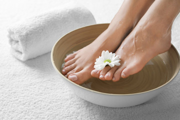 Closeup view of woman soaking her feet in dish with water and flower on white towel, space for text. Spa treatment