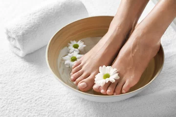 Poster Close-upmening van vrouw die haar voeten in schotel met water en bloemen op witte handdoek onderdompelen, ruimte voor tekst. Spa behandeling © New Africa