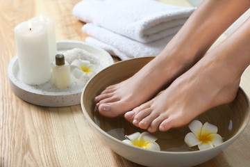 Obraz na płótnie Canvas Closeup view of woman soaking her feet in dish with water and flowers on wooden floor. Spa treatment