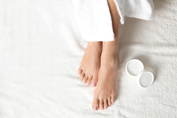 Top view of woman with beautiful feet and moisturizing cream on white towel, space for text. Spa...