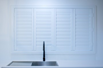 Closed plantation shutters and black kitchen sink mixer tap.