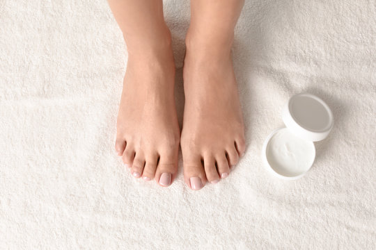 Woman with beautiful feet and jar of moisturizing cream on white towel, top view. Spa treatment