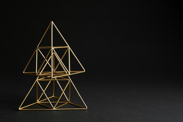 Shiny decorative gold pyramids on black background. Space for text
