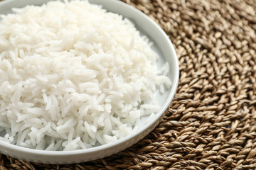 Plate of tasty cooked rice on wicker mat, closeup. Space for text