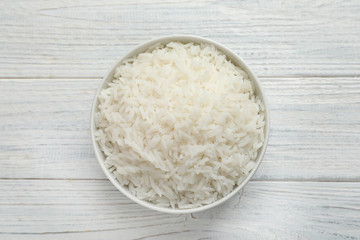 Bowl of tasty cooked rice on white wooden background, top view
