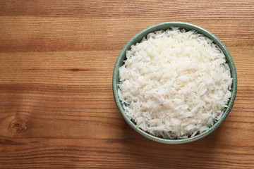 Bowl of tasty cooked rice on wooden background, top view. Space for text