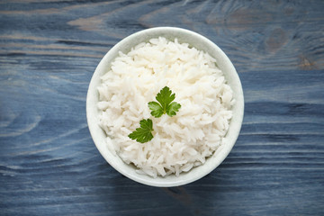 Bowl of tasty cooked rice with parsley on wooden background, top view