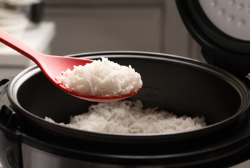 Spoon with tasty hot rice over cooker, closeup