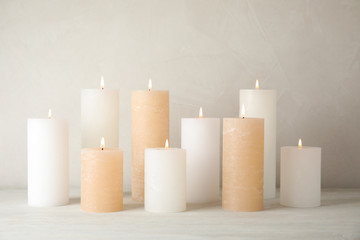 Burning candles on table against light background