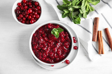 Flat lay composition with cranberry sauce in bowl on white wooden background