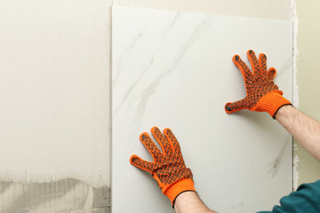 Man installing ceramic tile on wall, space for text. Building and renovation works