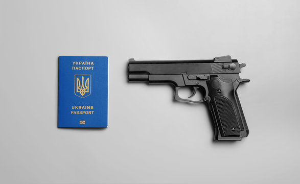 Gun with Ukrainian travel passport on grey background, flat lay