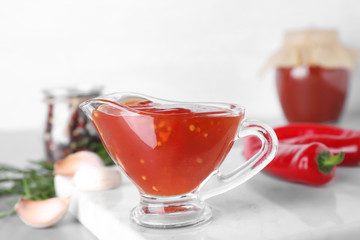 Gravy boat with hot chili sauce on table