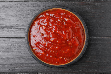 Bowl of hot chili sauce on dark wooden background, top view
