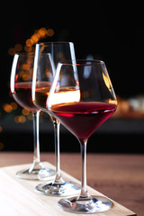 Glasses with different wines on wooden table against defocused lights