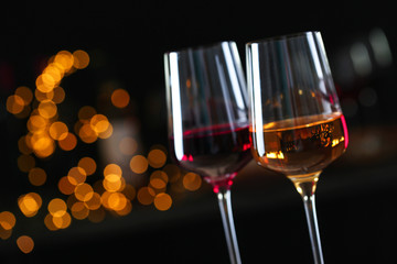 Glasses with different wines against defocused lights, closeup. Space for text