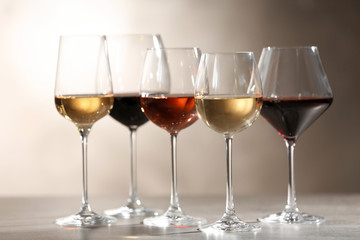 Glasses with different wines on grey table against light background