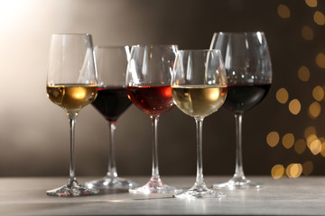 Glasses with different wines on grey table against defocused lights