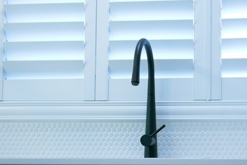Open plantation shutters and black kitchen sink mixer tap.