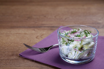 Glass bowl of vegetarian salad with cucumber and onion served on table. Space for text