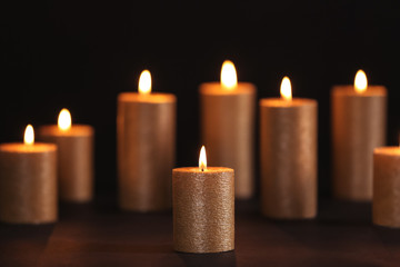 Fototapeta na wymiar Burning gold candles on table against black background, space for text