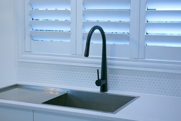 Open plantation shutters and black kitchen sink mixer tap.