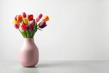 Vase with beautiful spring flowers on table against light background, space for text