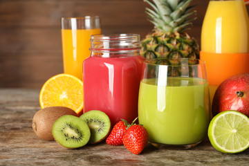 Glassware with different juices and fresh fruits on wooden background