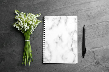 Notebook, pen and lily of the valley bouquet on grey background, flat lay. Space for text