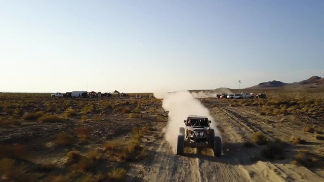Low aerial pull out shot of an off road vehicle speeding towards the camera on a desert race track.