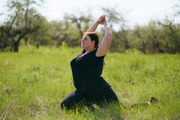 Body positive, yoga, confidence, high self esteem, meditating. Young calm overweight woman doing yoga at summer meadow. obesity, wellness, outdoor activity and health.