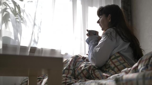 happy woman wakes up in the morning drinks coffee and looks out the window