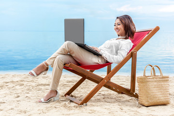 Asian business woman working with laptop sitting in the beach chair on beach