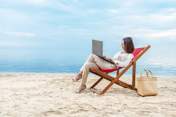 Asian business woman working with laptop sitting in the beach chair on beach