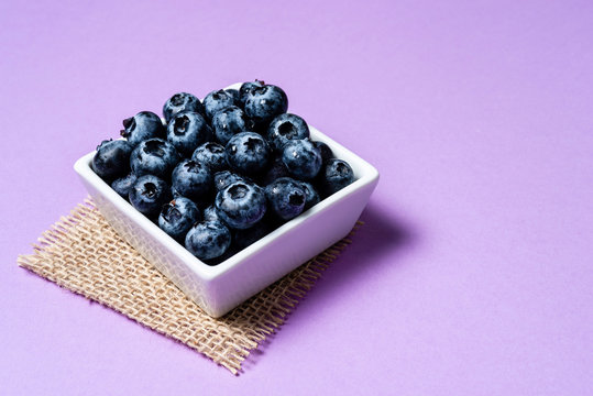 Fresh blueberries inside pot on purple background.