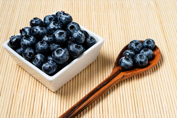 Fresh blueberries inside pot of white ceramic on bamboo background.