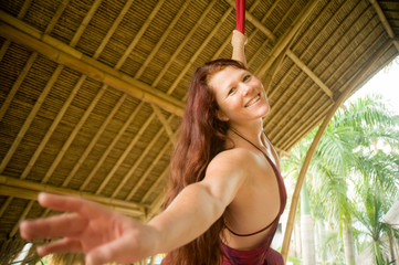  attractive and athletic aerialist woman hanging from silk fabric doing aerial dancing workout training happy at beautiful hut in artistic gymnastic balance exercise