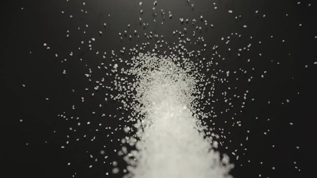 SLOW MOTION: White sea salt gains pouring onto a black table
