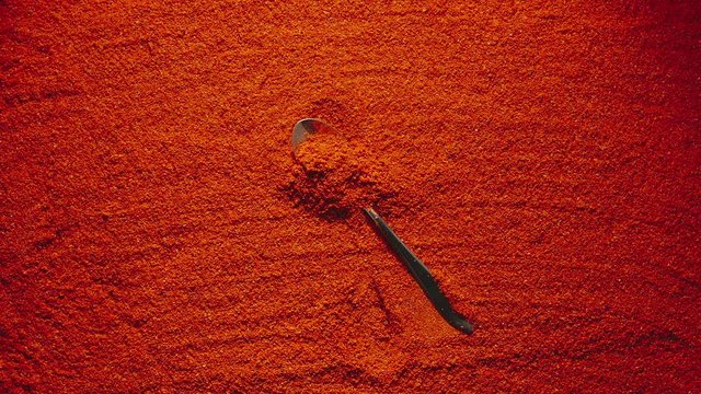 SLOW MOTION: Teaspoon with red pepper falls onto a heap of red pepper powder