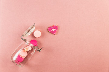 Pink french macarons or macaroons, and I love you cookie falling out of a glass jar over a pink table cloth background with copy space.