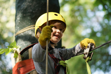 Happy child boy calling while climbing high tree and ropes. Happy little child climbing on a rope...