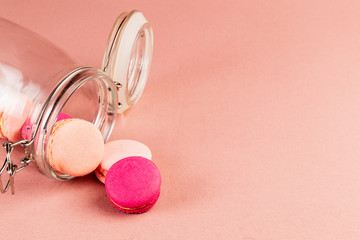 Light pink and fuchsia, magenta french macarons or macaroons, falling from a glass jar over a pink tablecloth with copyspace.