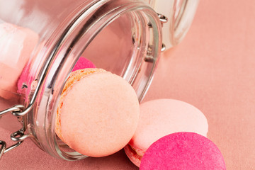Light pink and fuchsia pink french macarons or macaroons, falling from a glass jar over a pink tablecloth, closeup.