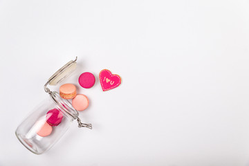 French pink and fuchsia macarons or macaroons, with I love you cookie falling out of a glass jar over a white background with large copyspace.